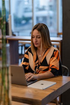 Focused woman in stylish attire working on her laptop in a modern cafe.