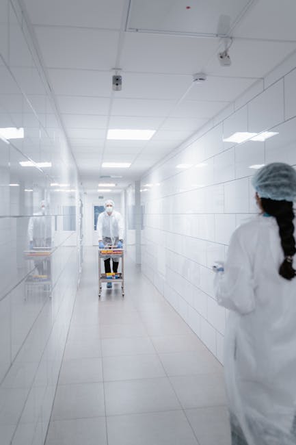 Medical personnel in protective clothing working in a sterile laboratory hallway.